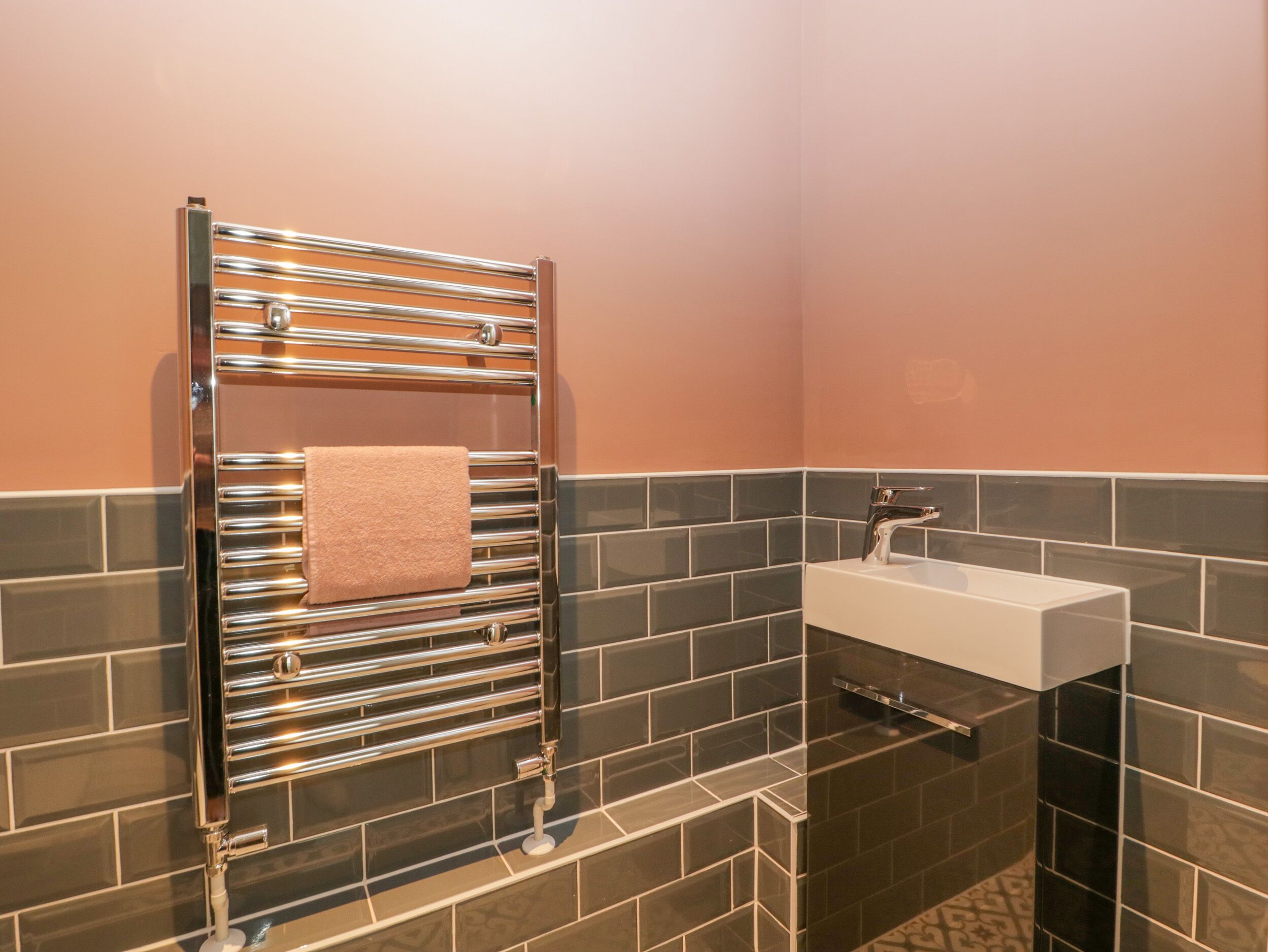 Un bagno con un porta asciugamani cromato che regge un asciugamano, un lavandino bianco e piastrelle scure alle pareti.
