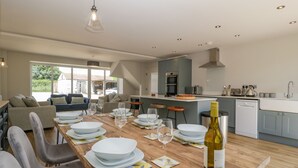 Cozinha moderna com área de jantar, apresentando uma mesa de madeira posta para uma refeição, uma garrafa de vinho e vista para o exterior.