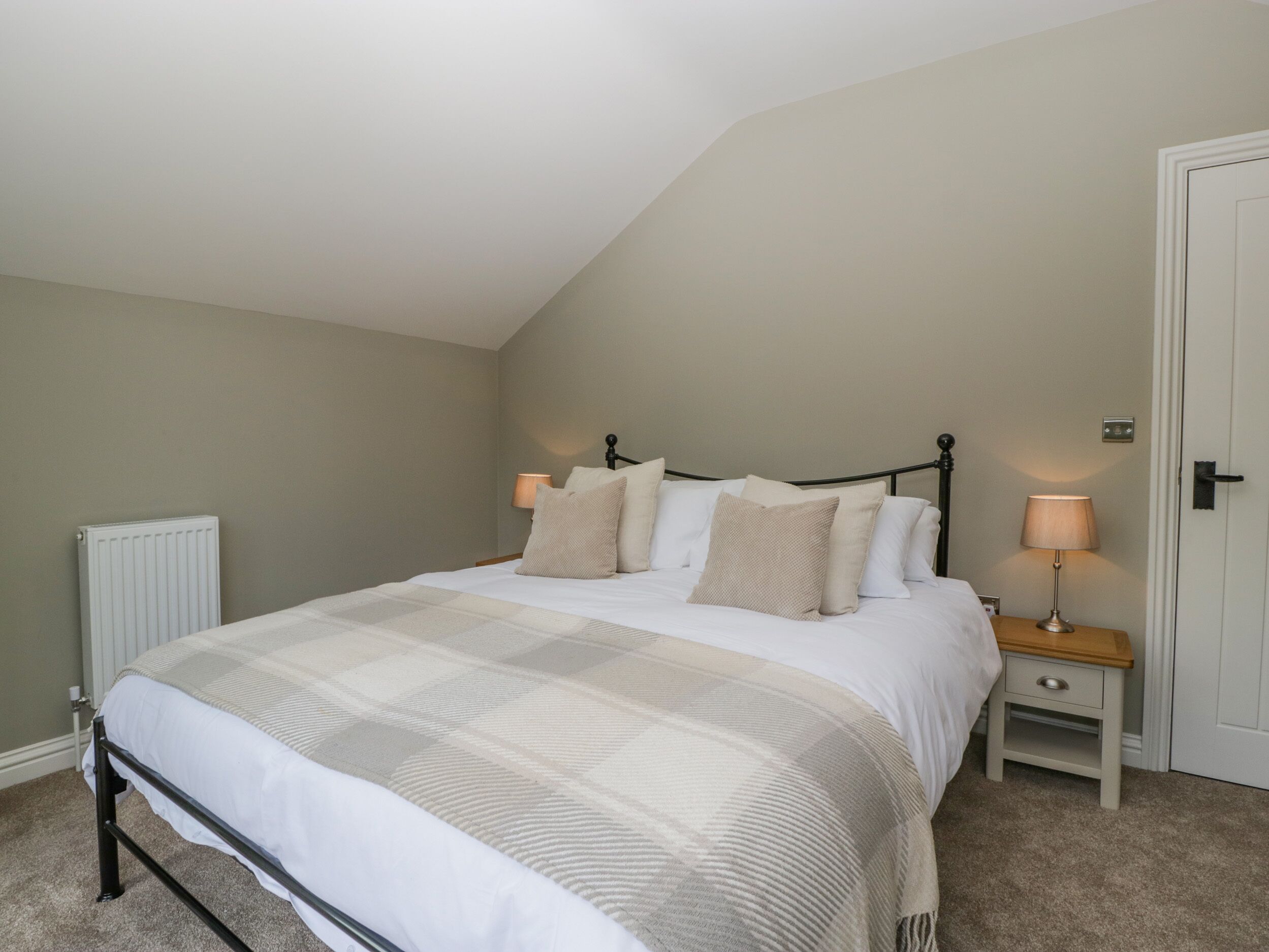 A bedroom with a bed, bedside tables, a radiator, and a door.