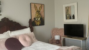 Een slaapkamer met een bed, een stoel, een televisie en kunstwerken aan de wanden.