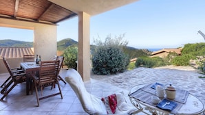 Eine überdachte Terrasse mit Tisch für zwei Personen, mit Blick auf eine malerische Landschaft mit Hügeln und blauem Himmel.