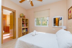 Une chambre à coucher avec un lit, une bibliothèque en bois, une fenêtre et un ventilateur de plafond.