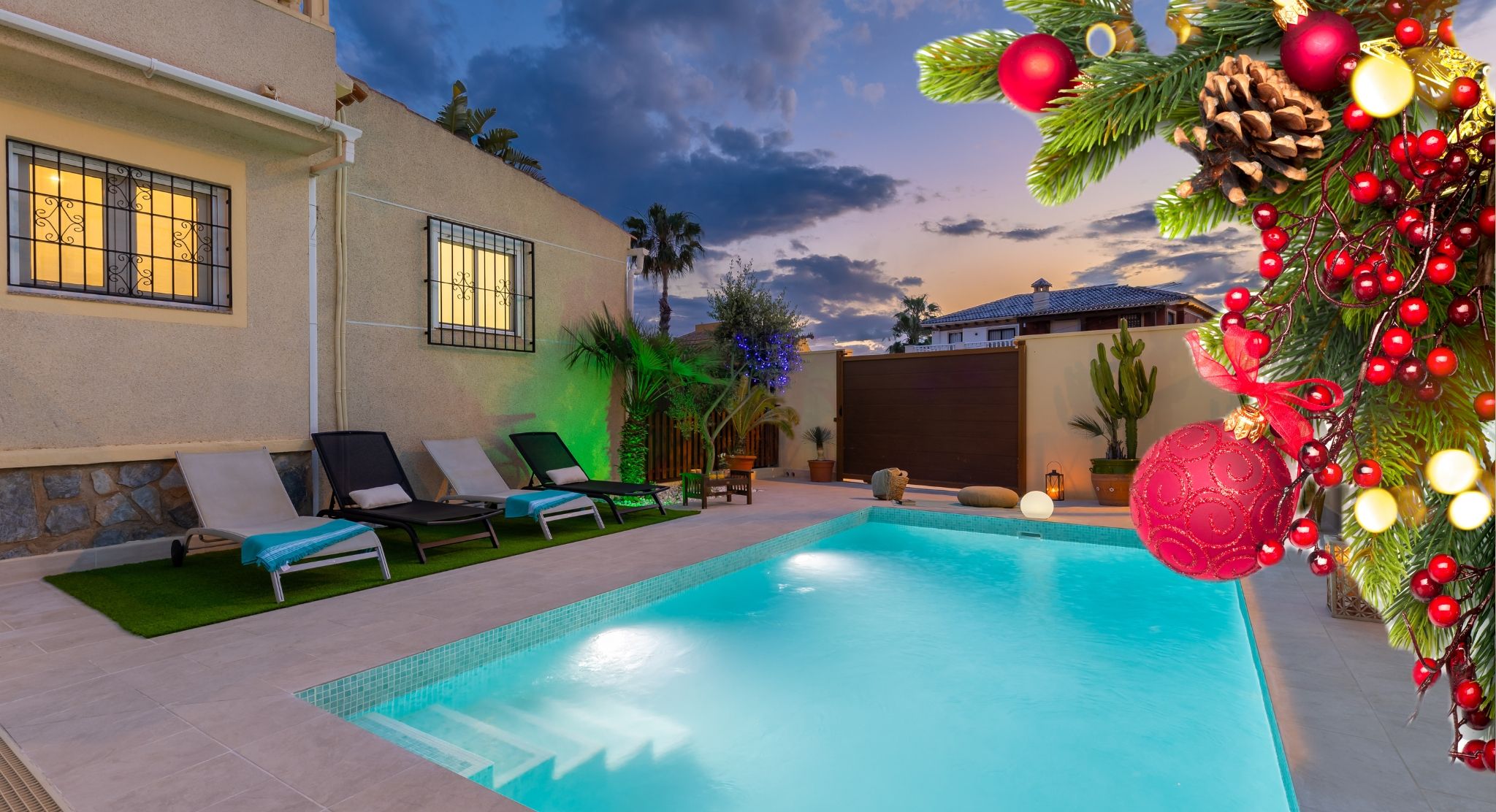 A swimming pool with lounge chairs, a cactus, and a Christmas tree with decorations.