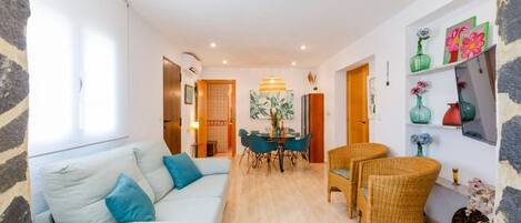 Una sala de estar moderna con sofá, mesa de comedor y sillas, una zona de cocina y un pasillo que conduce a otra habitación.