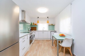 Una cocina compacta con muebles blancos, horno integrado, lavadora y un comedor con mesa y sillas.