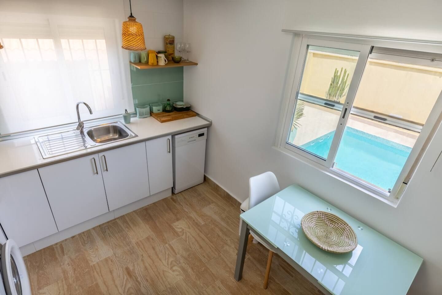Cocina compacta con lavabo, lavavajillas y ventana con vistas a una piscina.