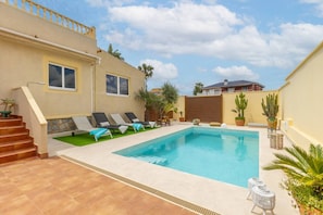 Una piscina con sillones de descanso, una escalera y un jardín con plantas en macetas.