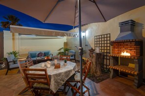 An outdoor patio with a table set for dining, surrounded by chairs, a brick oven, and a covered seating area.