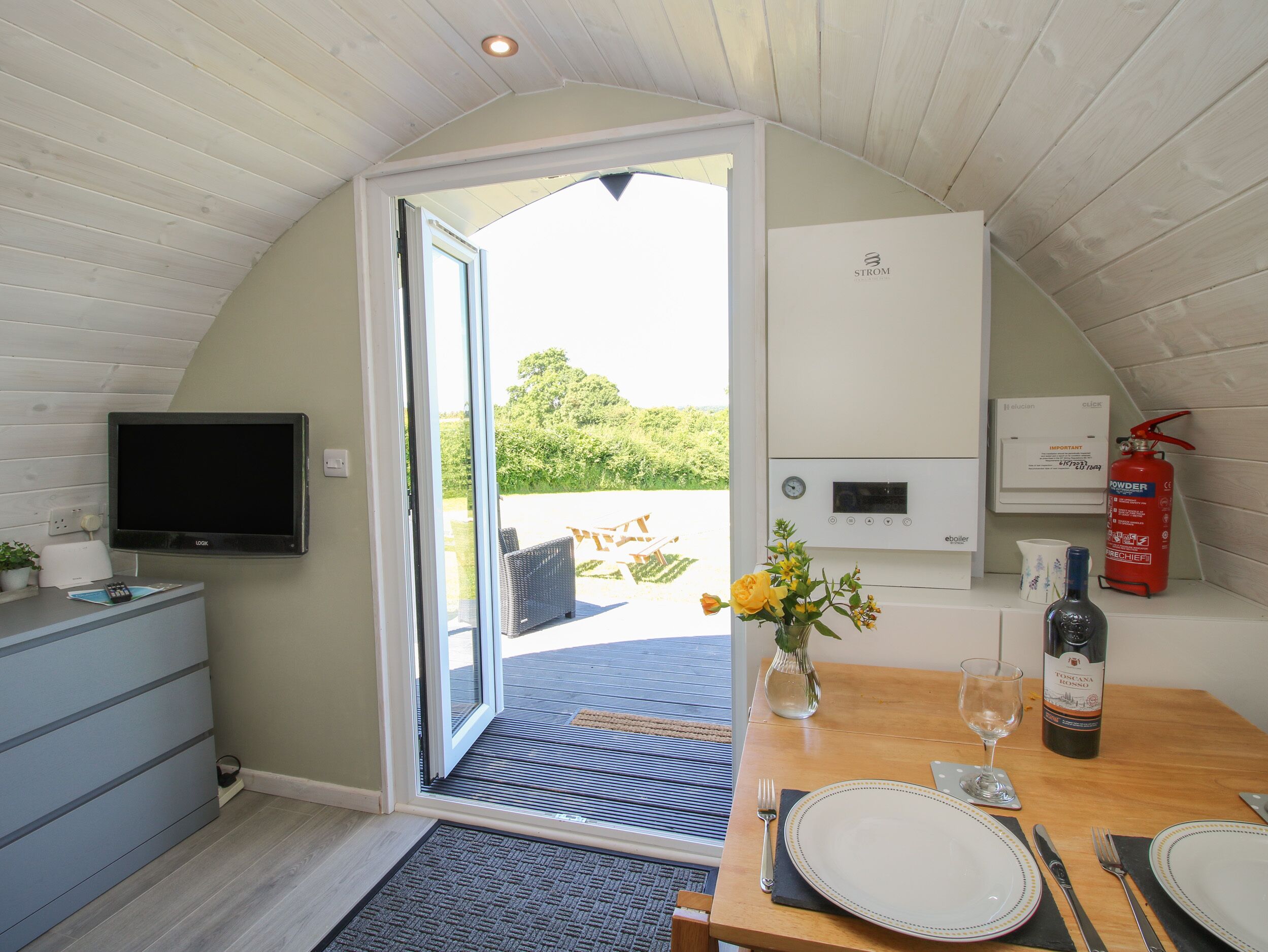 A modern kitchen with a built-in TV, a dining area with a table set for two, and a view of the outdoors.