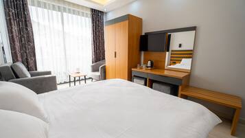 A hotel room with a large bed, a desk with a mirror, a chair, and a small table.