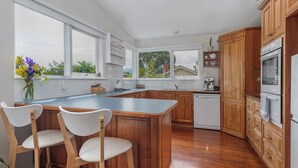 A modern kitchen with wooden cabinets, a large island, and a view of the outdoors. - Lynmouth Cottage - a cosy home away from home (New Town)