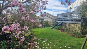 A backyard with a lawn, a wooden fence, and a house with a garage. - Lynmouth Cottage - a cosy home away from home (New Town)