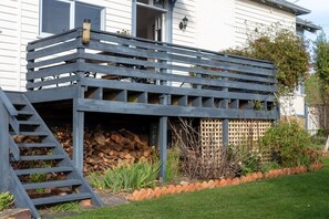 Une maison avec une terrasse en bois, un escalier menant à une zone abritée et une pile de bois de chauffage.