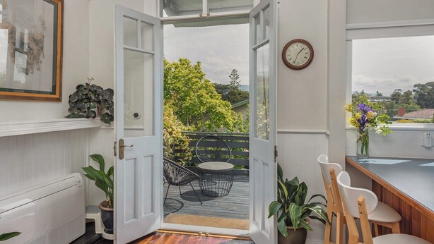 An open door leading to a deck with outdoor furniture, a clock on the wall, and a potted plant on the left. - Lynmouth Cottage - a cosy home away from home (New Town)