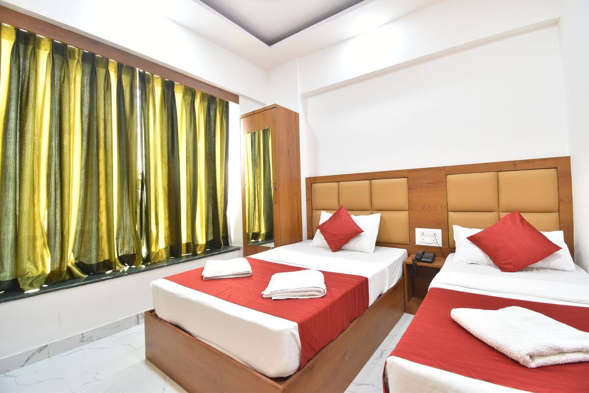 A hotel room with two beds, a wooden headboard, a nightstand, and a window with curtains.