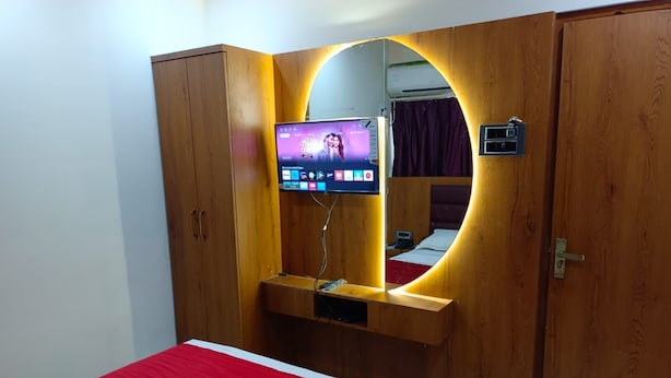 A bedroom with a bed, a TV mounted on a wooden cabinet, and a mirror. - HOTEL AIRPORT ANNEX (Mumbai)