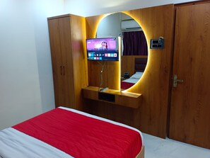 A bedroom with a bed, a TV mounted on a wooden cabinet, and a mirror. - HOTEL AIRPORT ANNEX (Mumbai)