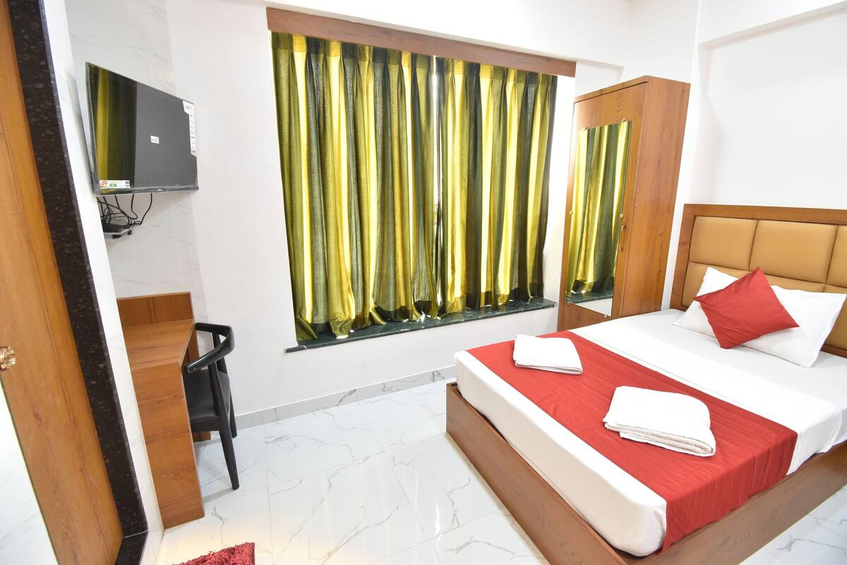 A hotel room with a bed, a desk, a chair, a TV, and a window with curtains.
