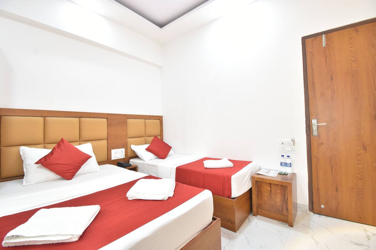 A hotel room with two beds, each with red bedding and white pillows, a wooden headboard, a small wooden side table with a water bottle, and a wooden door.
