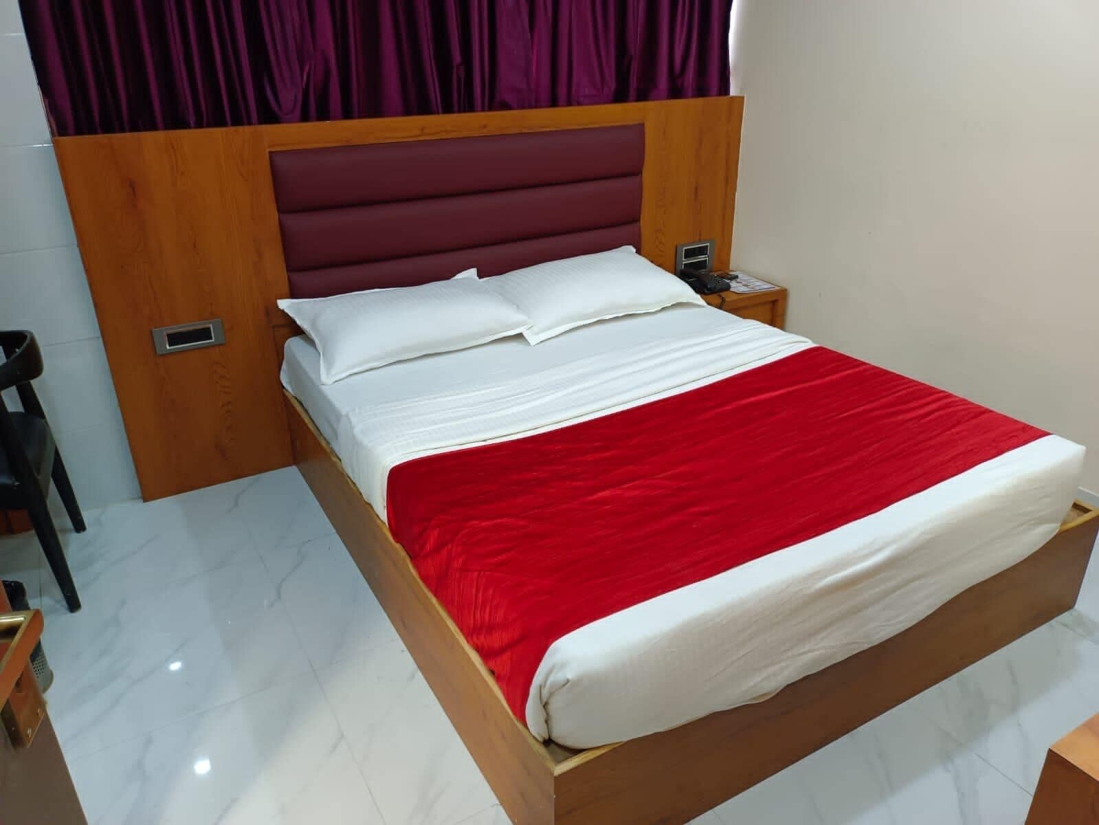 Habitación individual con una cama de madera, ropa de cama blanca y una manta roja.