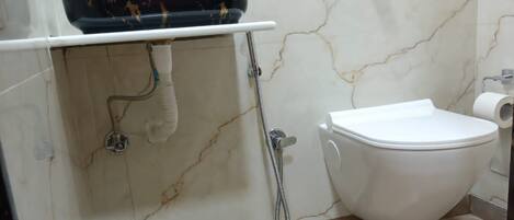 Un baño con pared de mármol, un lavamanos negro con dispensador de jabón morado, un inodoro blanco y un cabezal de ducha.