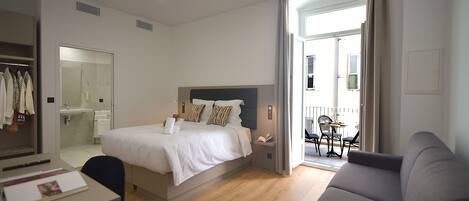 Habitación de hotel con cama, escritorio, silla, sofá, baño y balcón con mesa y sillas.