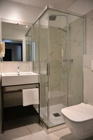 Un baño moderno con ducha envuelta en vidrio, un lavabo blanco y un inodoro independiente.