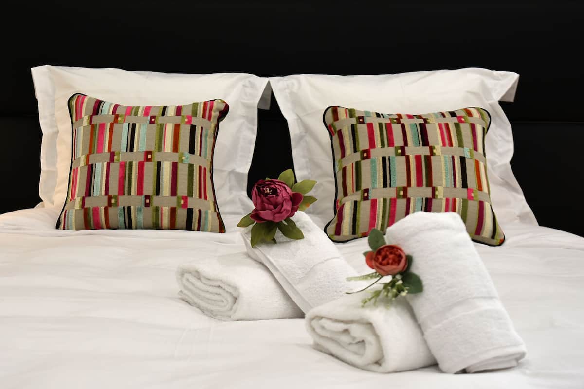 A neatly made bed with two striped pillows, a folded white towel, and a single red rose.