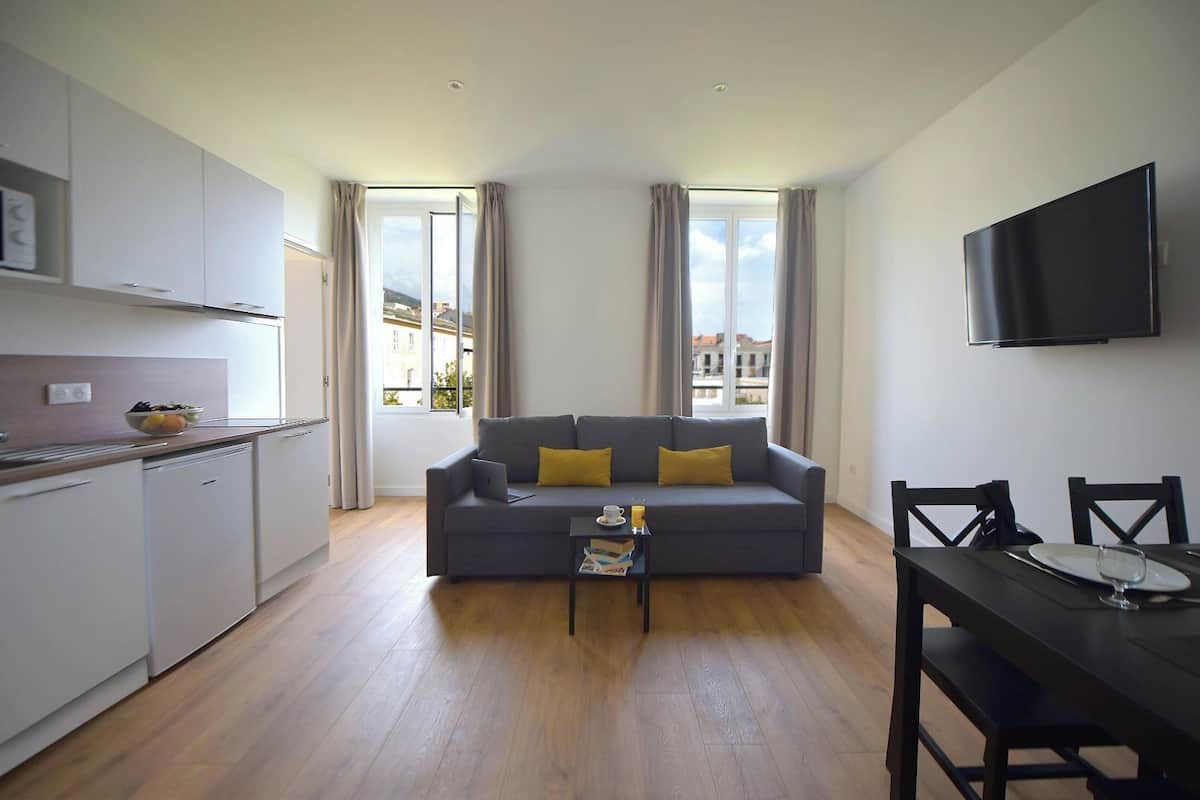 A modern apartment with a grey sofa, a dining table, and a kitchen area.