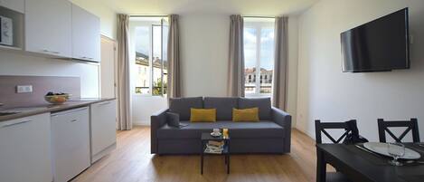 Un apartamento moderno con un sofá gris, una mesa de comedor y una zona de cocina.