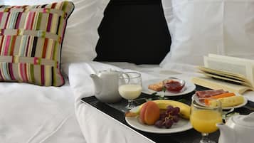 Un plateau de petit-déjeuner soigneusement préparé est posé sur un lit, à côté d’un oreiller, d’un livre et d’un autre plateau contenant des fruits, du fromage et des œufs.