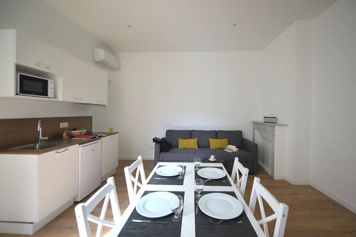 A compact living space with a kitchenette, dining area, and a sofa with cushions.