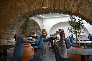 Un comedor interior con paredes de piedra, sillas azules y macetas de terracota con plantas.