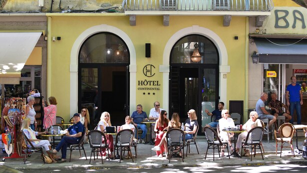 Ein Café im Freien vor einem Hotel mit Außenbestuhlung und einem sichtbaren Eingang.
