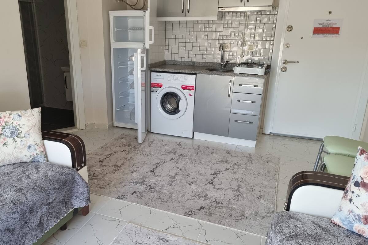 Un espacio habitable compacto con sofá, una pequeña mesa de comedor, lavadora y kitchenette.