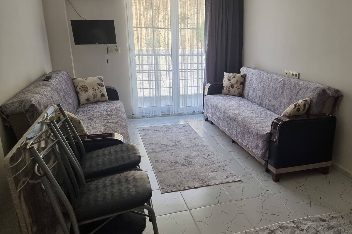 Sala de estar con dos sofás, un televisor montado en la pared y un ventanal con cortinas.
