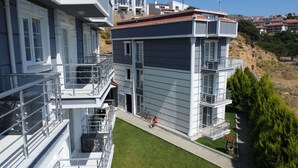 A multi-story residential building with balconies, a small lawn, and a hilly backdrop. - Sidelya Apart (Gökçeada)