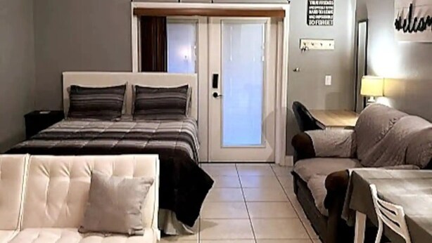 Een slaapkamer met een bed, een bank, een bureau en een schuifdeur naar een balkon.