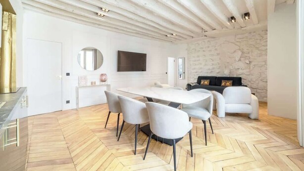 A modern dining area with a large table, white chairs, and a stone wall. - A Breathtaking  2BR/2BA in Le Marais (Paris)