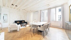 A modern living room with a white sofa, a dining table with chairs, and a herringbone wooden floor. - A Breathtaking  2BR/2BA in Le Marais (Paris)