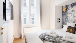 A hotel room with a large bed, a window with curtains, a wall with a textured mural, and a flat-screen TV mounted on the wall. - A Breathtaking  2BR/2BA in Le Marais (Paris)