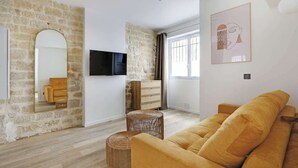 A modern living room with a stone wall, a sofa, a television, and a framed artwork. - A Chic 1-BR in Sentier - Montorgueil (Paris)