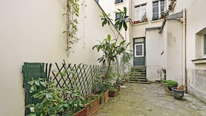 A narrow alleyway with a stone floor, bordered by a wooden fence and potted plants. - A Chic 1-BR in Sentier - Montorgueil (Paris)