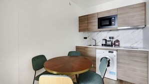 A compact kitchen with a microwave, coffee maker, and washing machine. There is a round wooden table with four chairs. - A Chic 1-BR in Sentier - Montorgueil (Paris)
