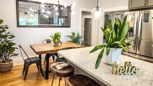 A modern kitchen with a marble countertop, stainless steel appliances, and a dining area with wooden chairs and a table.