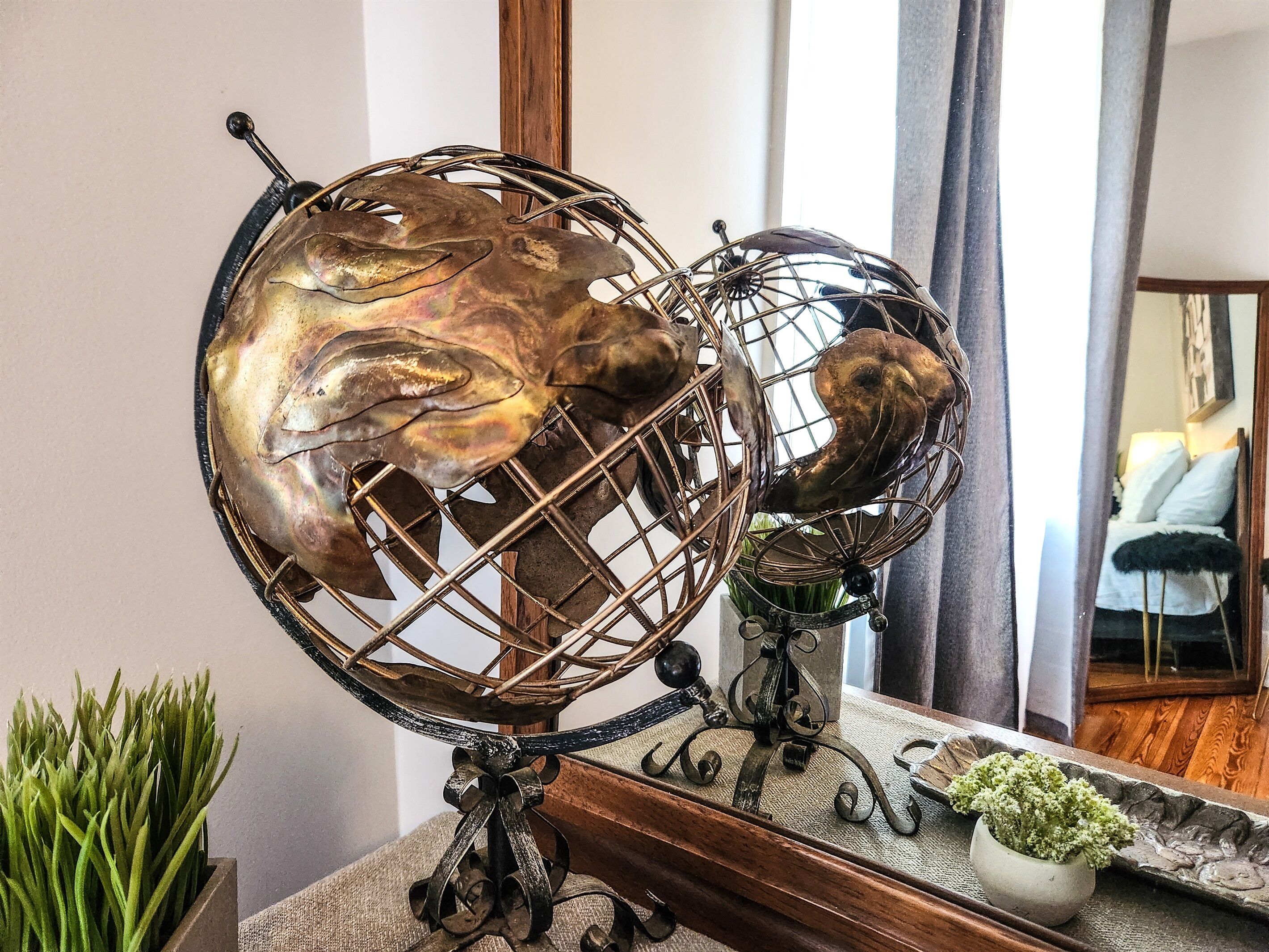 Une sculpture en forme de globe, posée sur un socle en bois, avec un miroir qui reflète l’intérieur d’une pièce.
