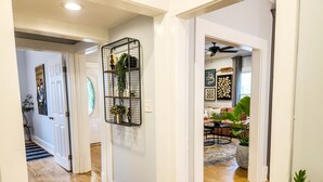 A hallway with a black metal shelf holding plants, a white door, and a wooden floor.