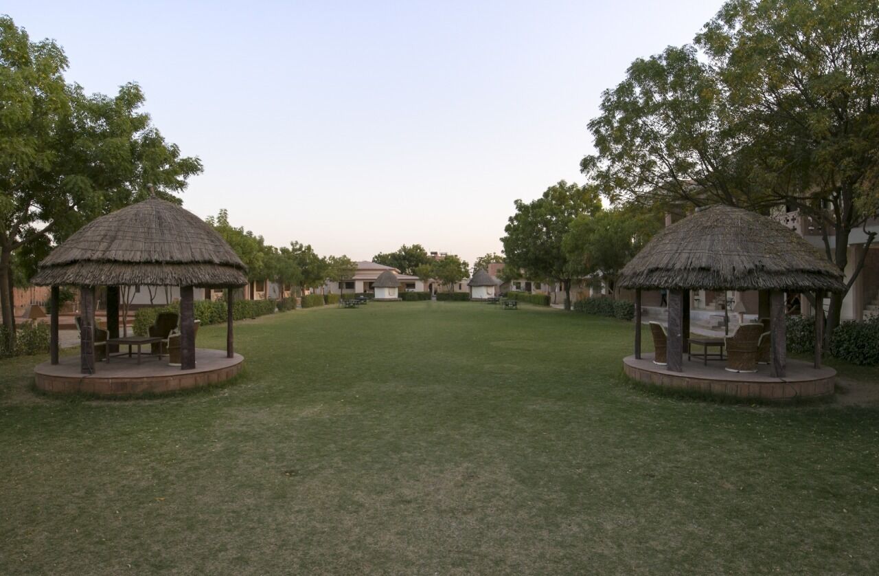 Un patio con dos pabellones de techo de paja, rodeado de árboles y césped.