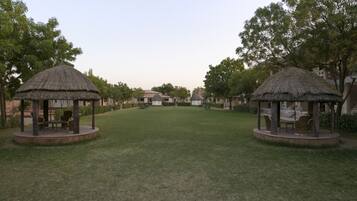 A courtyard with two thatched-roof gazebos, surrounded by trees and grass.