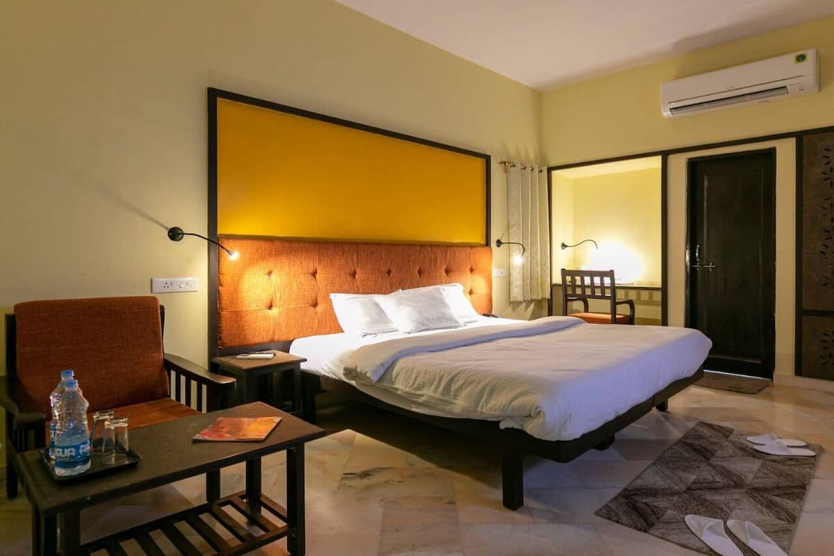 Quarto de hotel com cama, uma cadeira, uma mesa com garrafa e copos, e um ar condicionado.